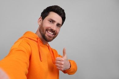 Photo of Smiling man taking selfie and showing thumbs up on grey background, space for text
