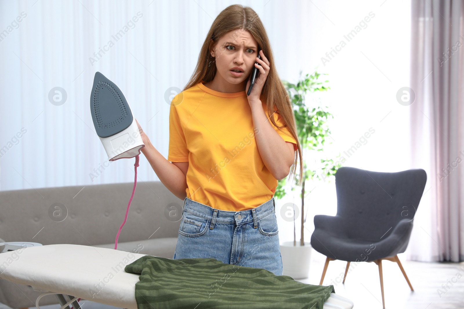 Photo of Emotional woman talking on phone while ironing clothes at home