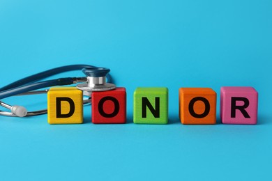 Photo of Word Donor made of colorful wooden cubes and stethoscope on light blue background