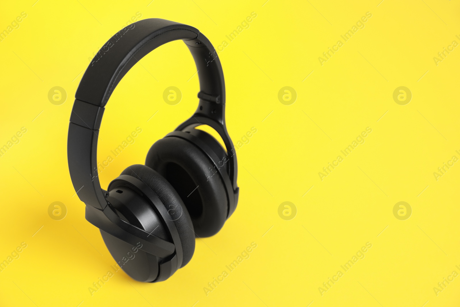 Photo of Modern wireless headphones on yellow background. Space for text