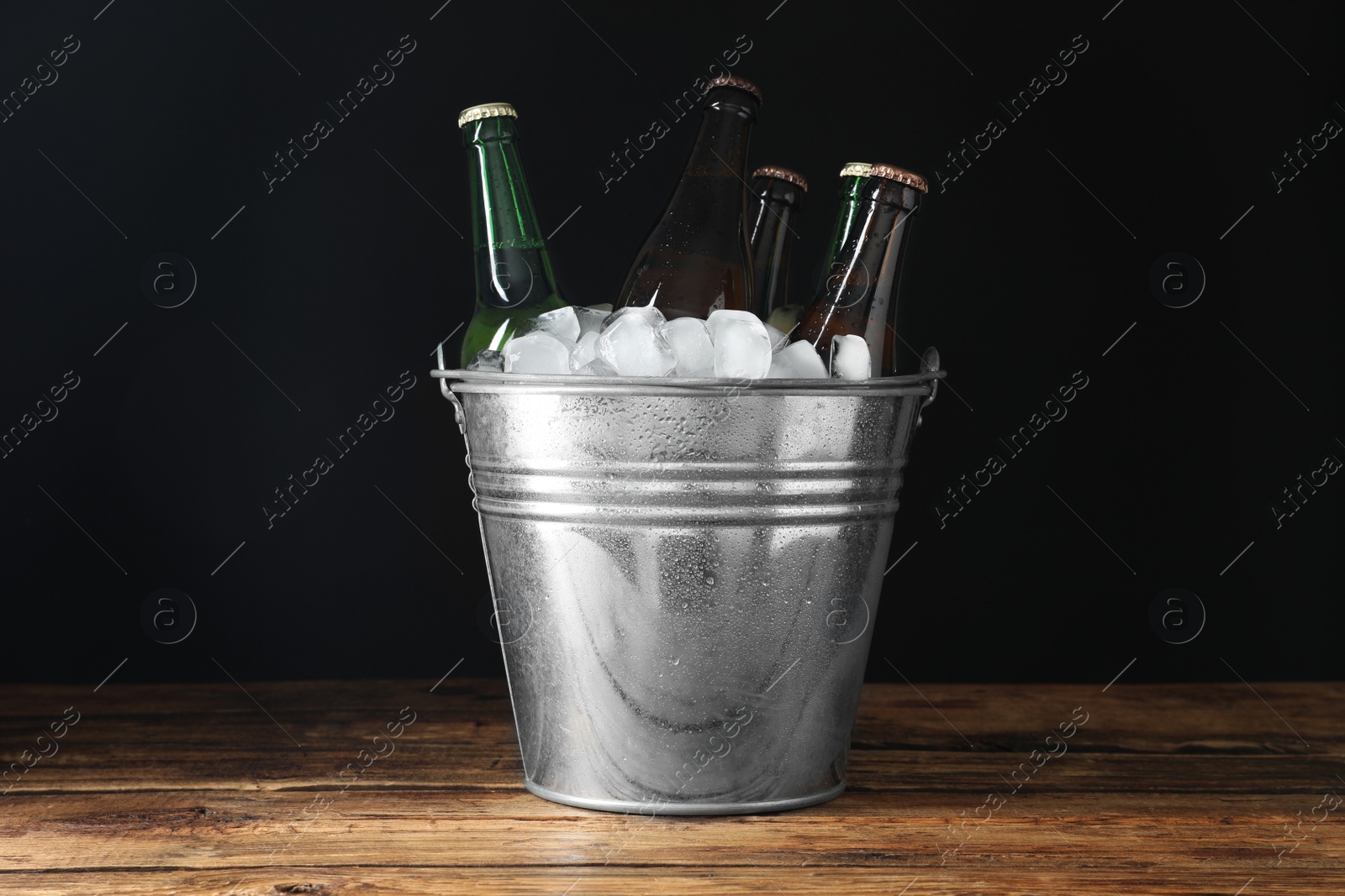 Photo of Metal bucket with bottles of beer and ice cubes on wooden table