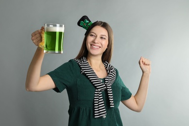 Happy woman in St Patrick's Day outfit with beer on light grey background