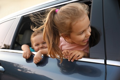 Photo of Happy little kids looking from family car outdoors