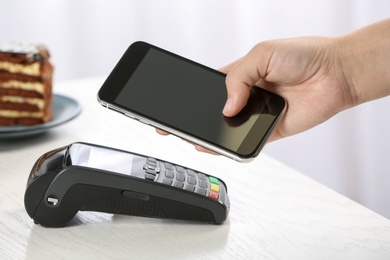 Woman using terminal for contactless payment with smartphone in cafe