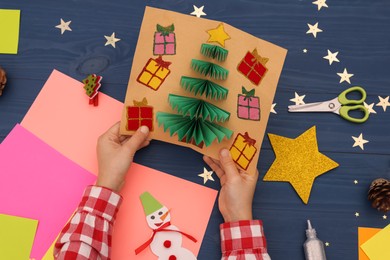 Photo of Little child with beautiful Christmas card at blue wooden table, top view