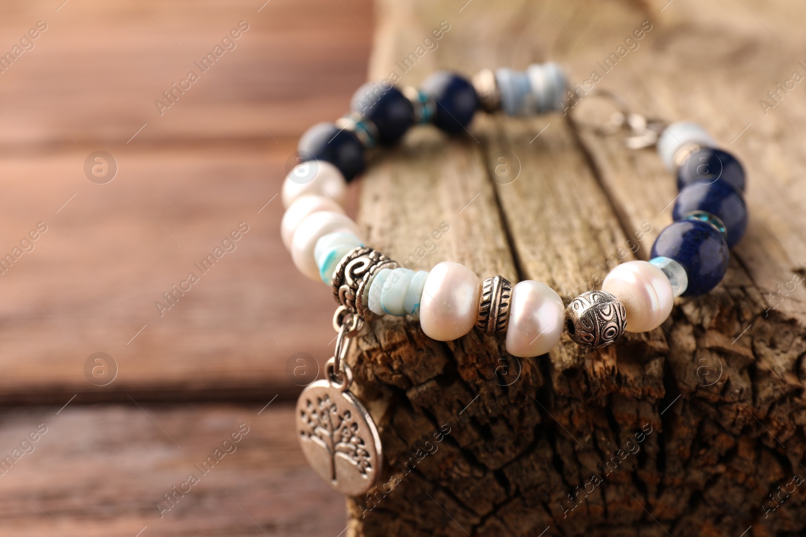 Photo of Beautiful bracelet with gemstones and decorative piece of wood on table, closeup. Space for text