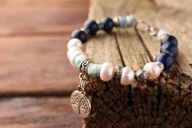 Photo of Beautiful bracelet with gemstones and decorative piece of wood on table, closeup. Space for text