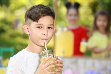 Photo of Cute little boy drinking natural lemonade in park, space for text. Summer refreshing beverage