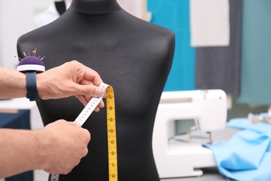 Photo of Designer with measuring tape near mannequin in tailor workshop, closeup