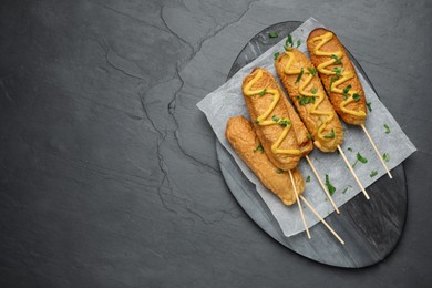 Photo of Delicious deep fried corn dogs with mustard and parsley on black table, top view. Space for text