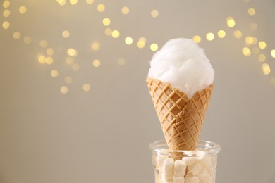 Sweet cotton candy in waffle cone against blurred lights, closeup. Space for text