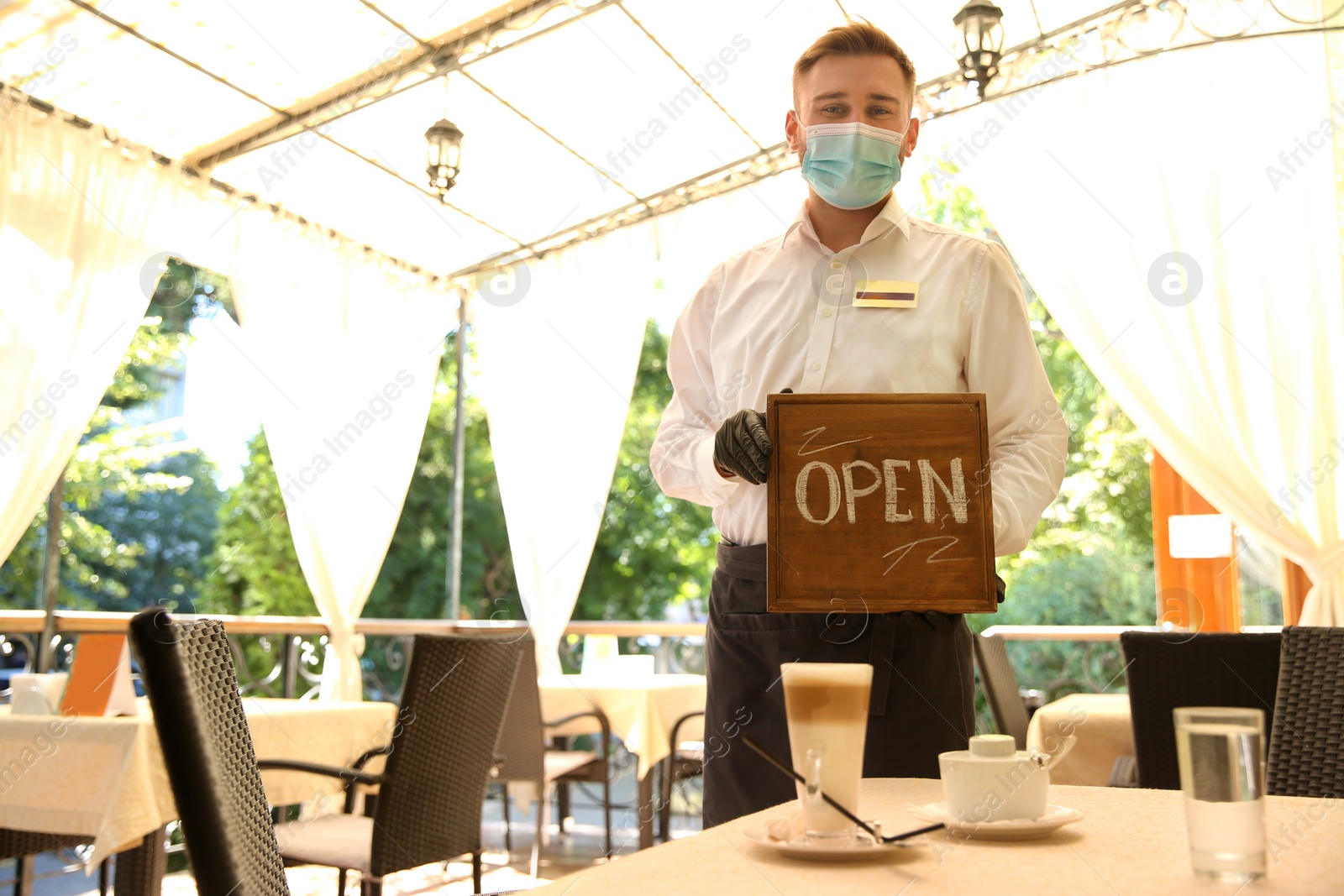 Photo of Waiter holding OPEN sign in restaurant. Catering during coronavirus quarantine