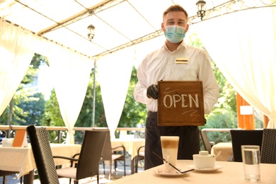 Waiter holding OPEN sign in restaurant. Catering during coronavirus quarantine