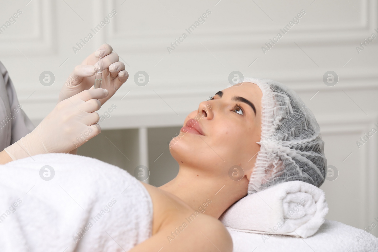 Photo of Professional cosmetologist holding skincare ampoule while working with client in clinic, closeup