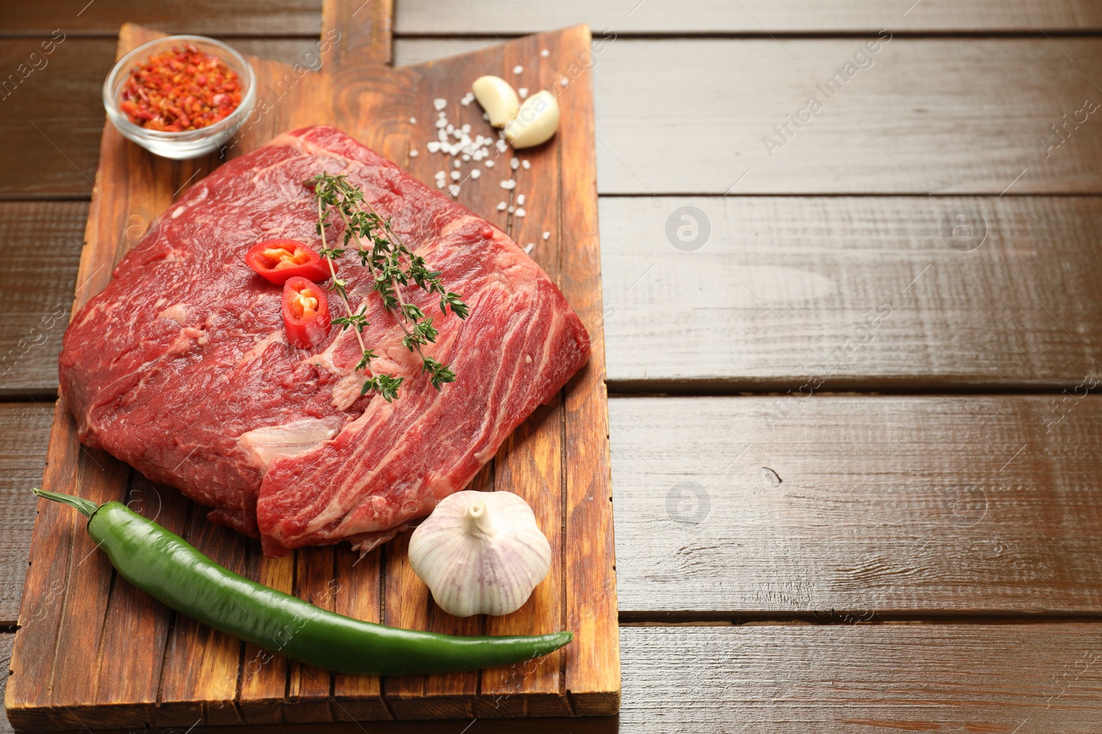 Photo of Fresh raw beef cut with spices on wooden table. Space for text