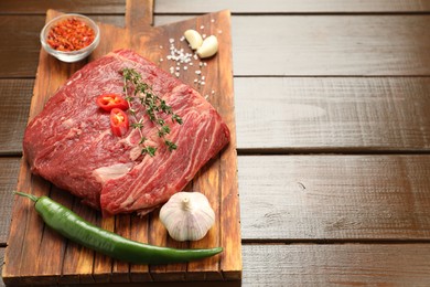 Fresh raw beef cut with spices on wooden table. Space for text