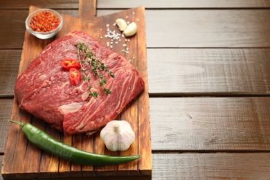 Photo of Fresh raw beef cut with spices on wooden table. Space for text