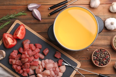 Flat lay composition with fondue pot, raw meat, vegetables and spices on wooden background