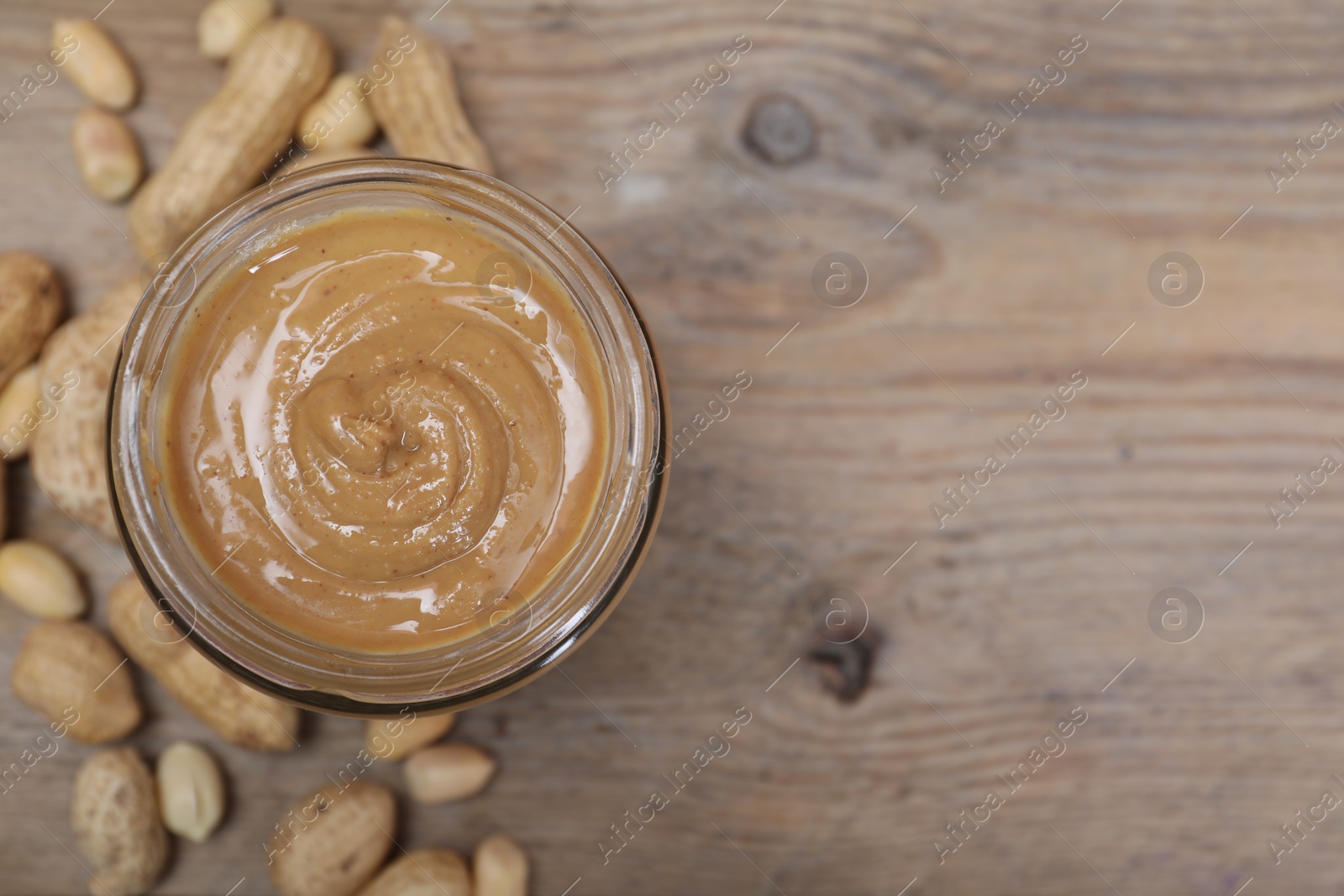 Photo of Tasty peanut nut paste in jar on wooden table, top view. Space for text