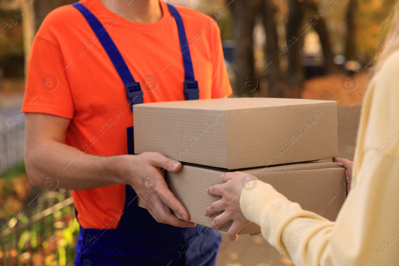 Photo of Woman receiving parcels from courier in uniform outdoors, closeup