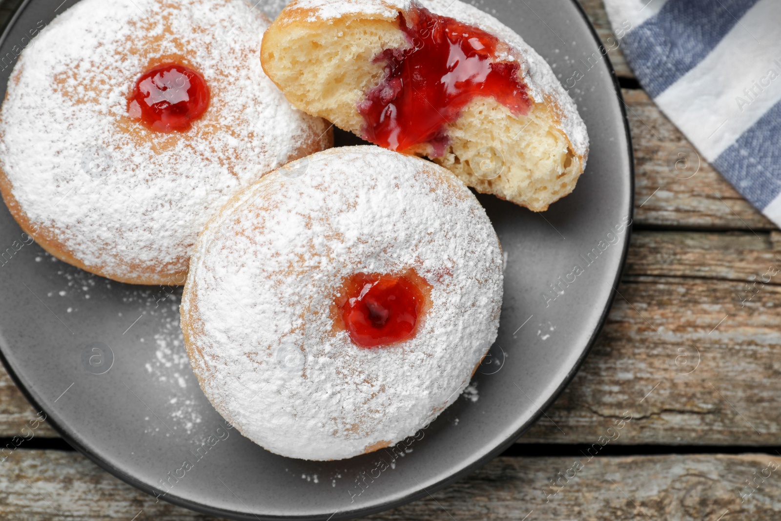 Photo of Delicious donuts with jelly and powdered sugar on wooden table, top view