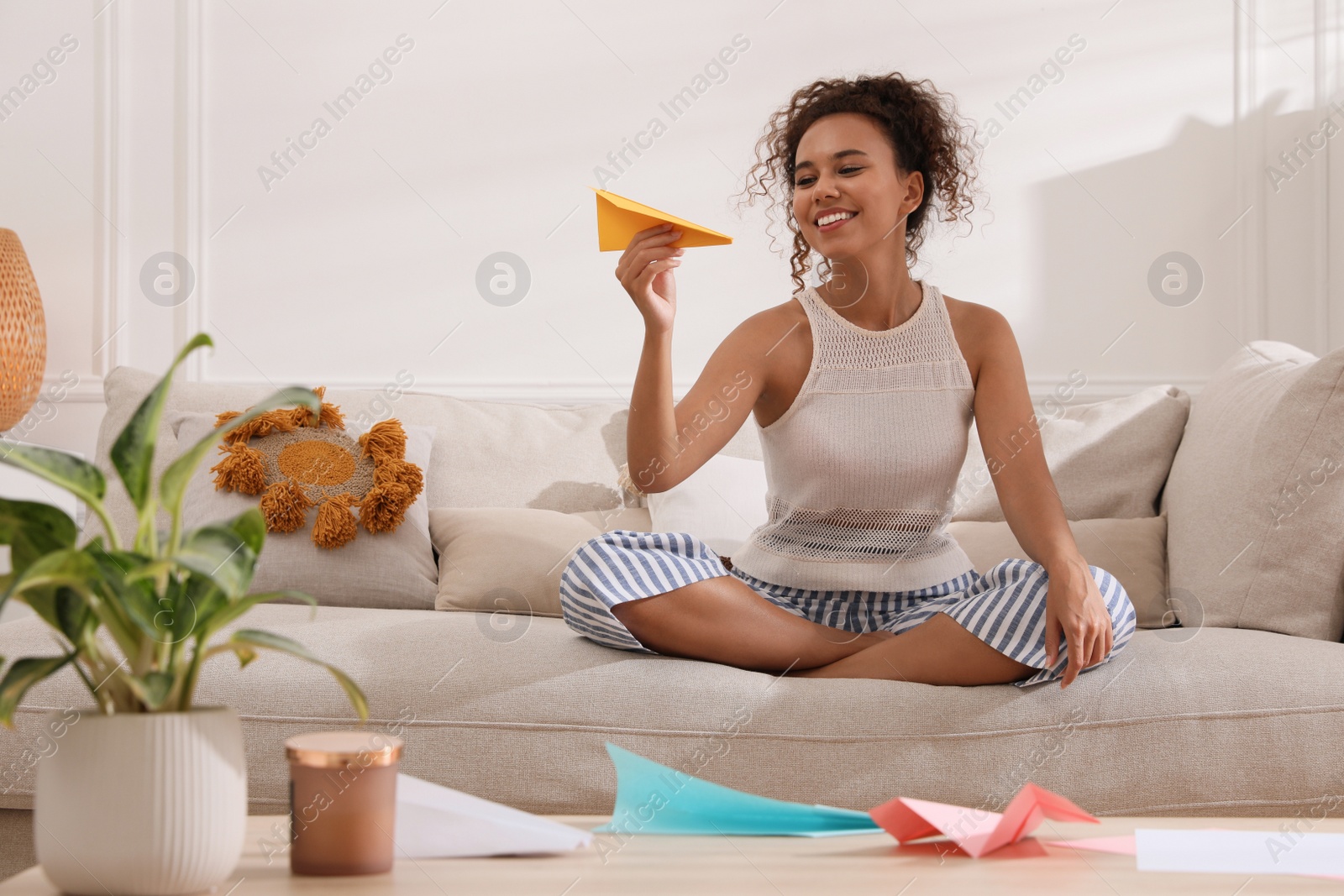 Photo of Beautiful African-American woman playing with paper plane in living room at home