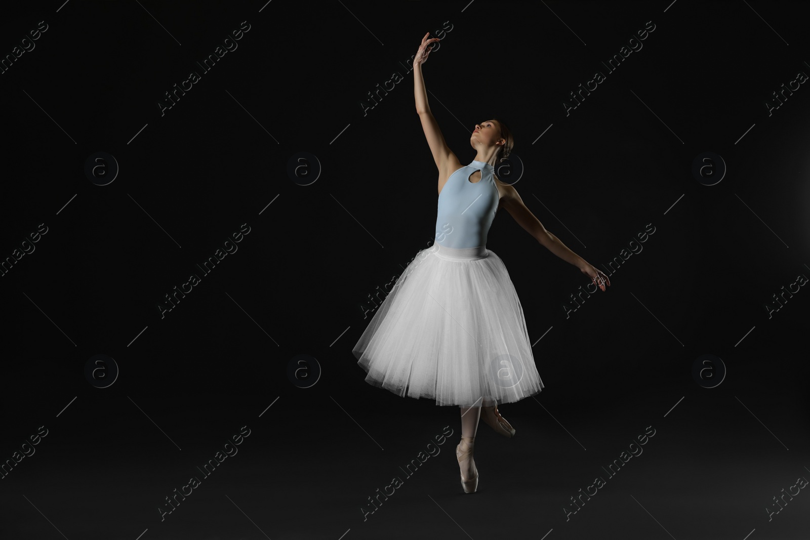 Photo of Young ballerina practicing dance moves on black background. Space for text