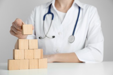 Photo of Doctor building pyramid of blank wooden cubes on white table against light background, closeup. Space for text