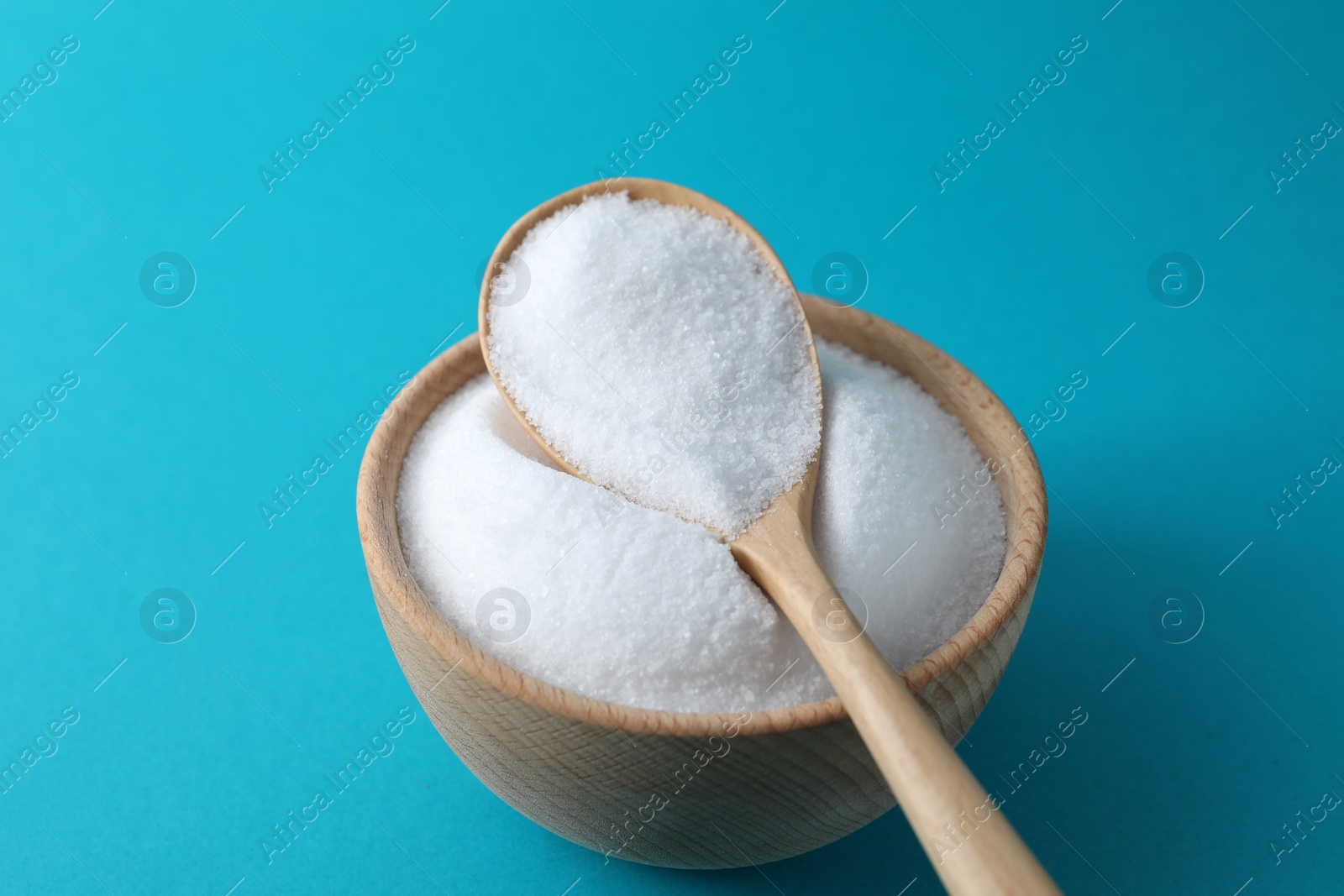 Photo of Organic white salt in bowl and spoon on light blue background, closeup