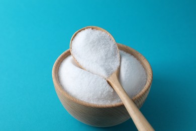 Photo of Organic white salt in bowl and spoon on light blue background, closeup