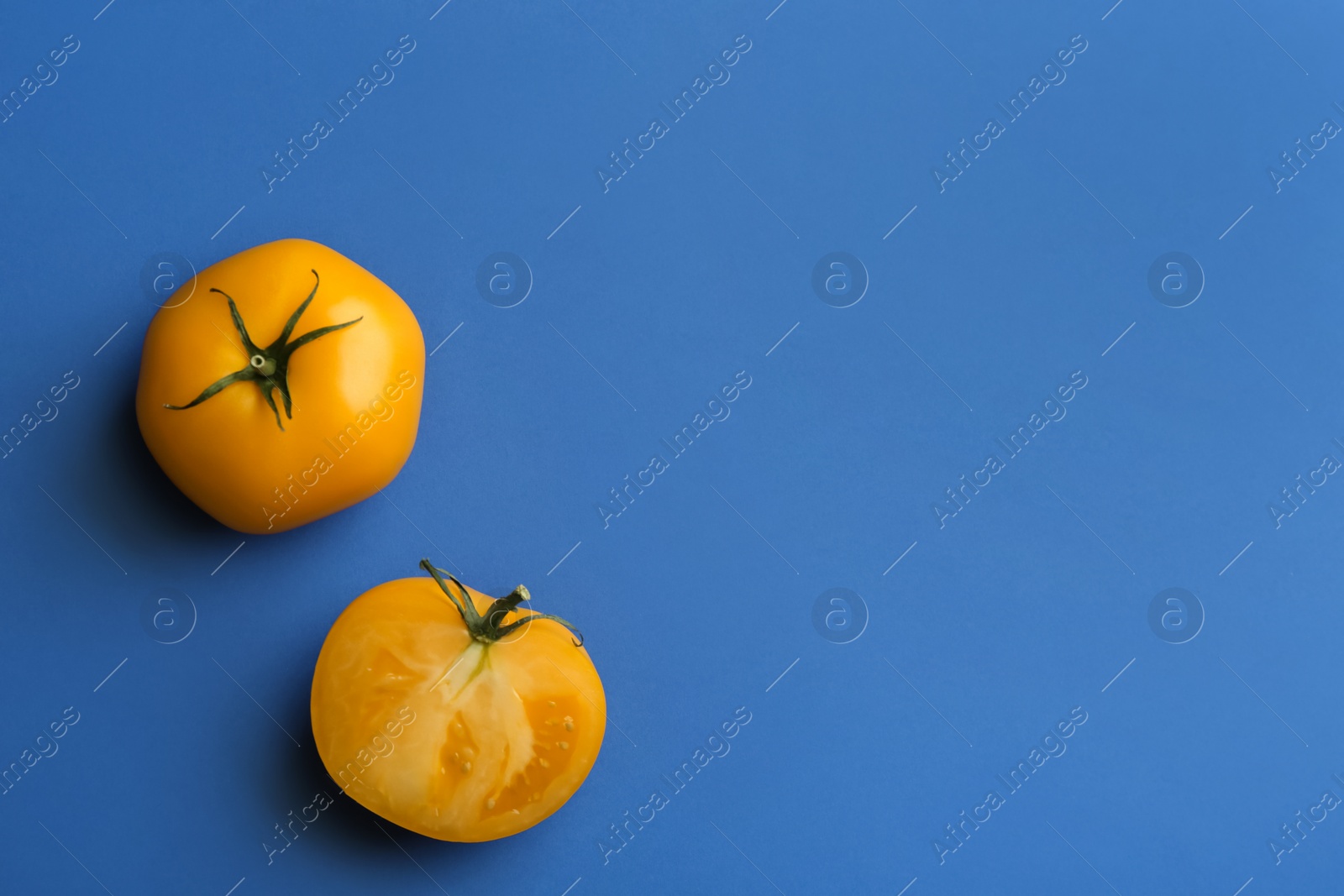 Photo of Whole and cut yellow tomatoes on blue background, flat lay. Space for text