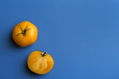 Photo of Whole and cut yellow tomatoes on blue background, flat lay. Space for text