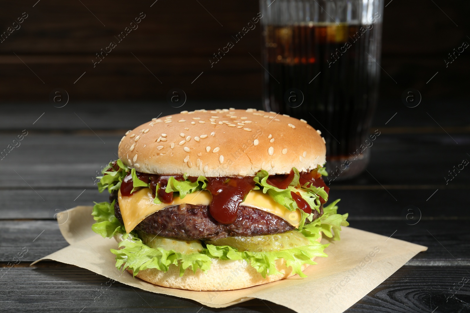 Photo of Burger with delicious patty and soda drink on black wooden table