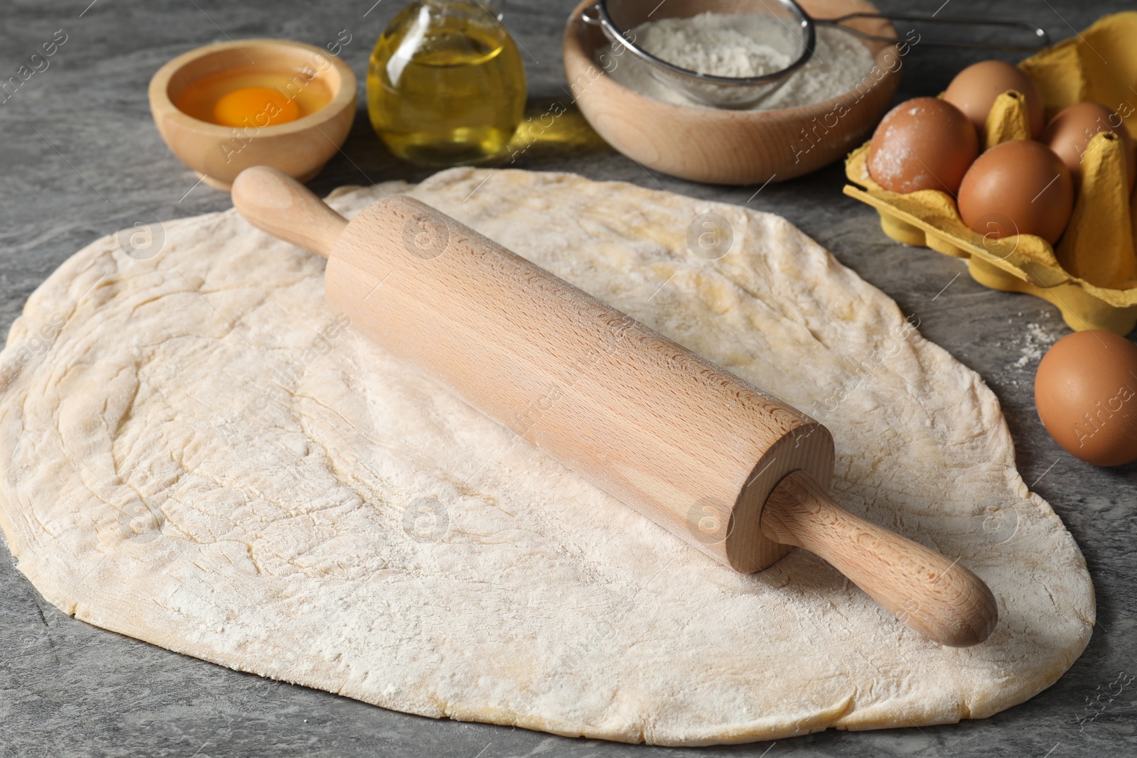 Photo of Raw dough, rolling pin and ingredients on grey table