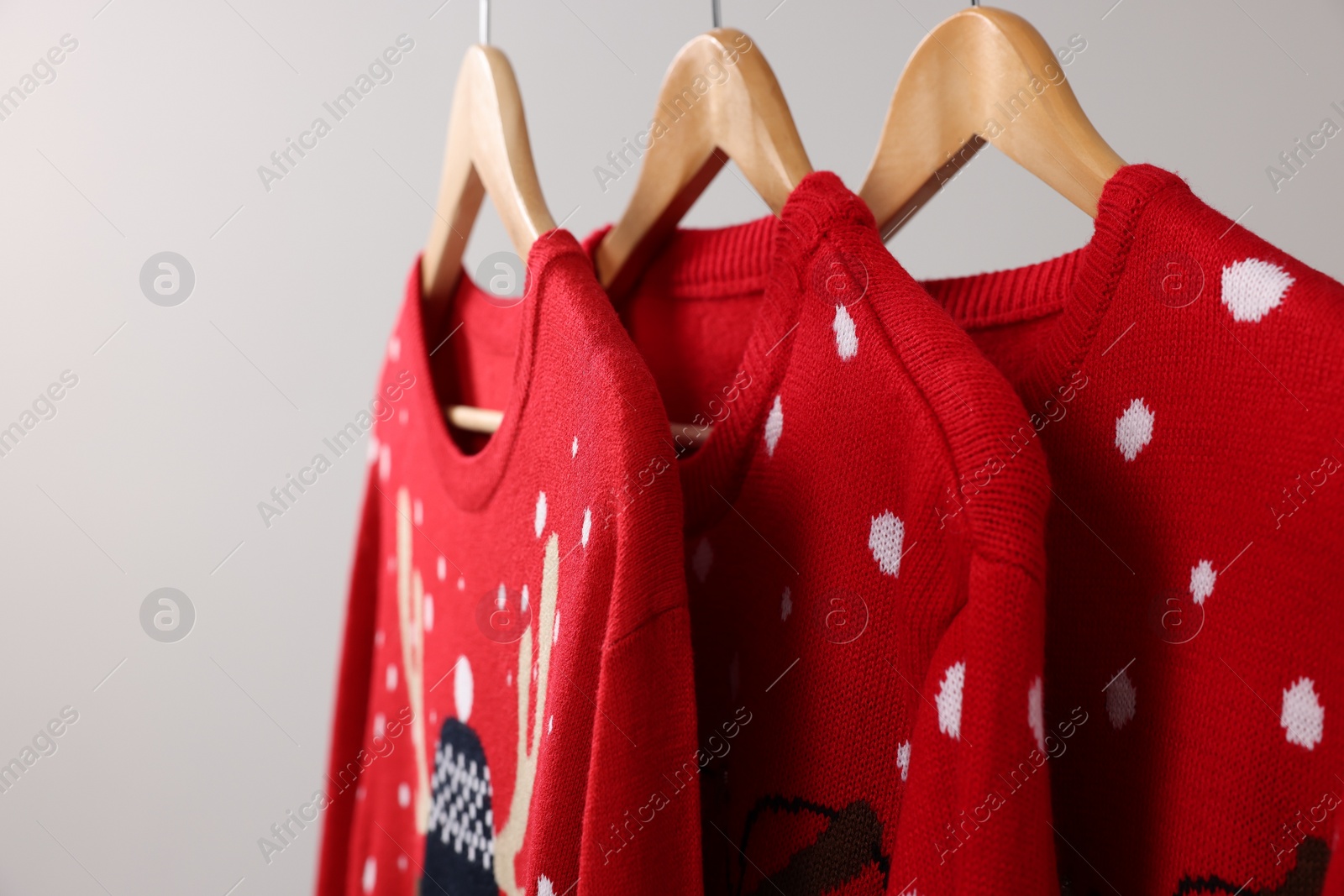 Photo of Different Christmas sweaters hanging on rack against light background, closeup