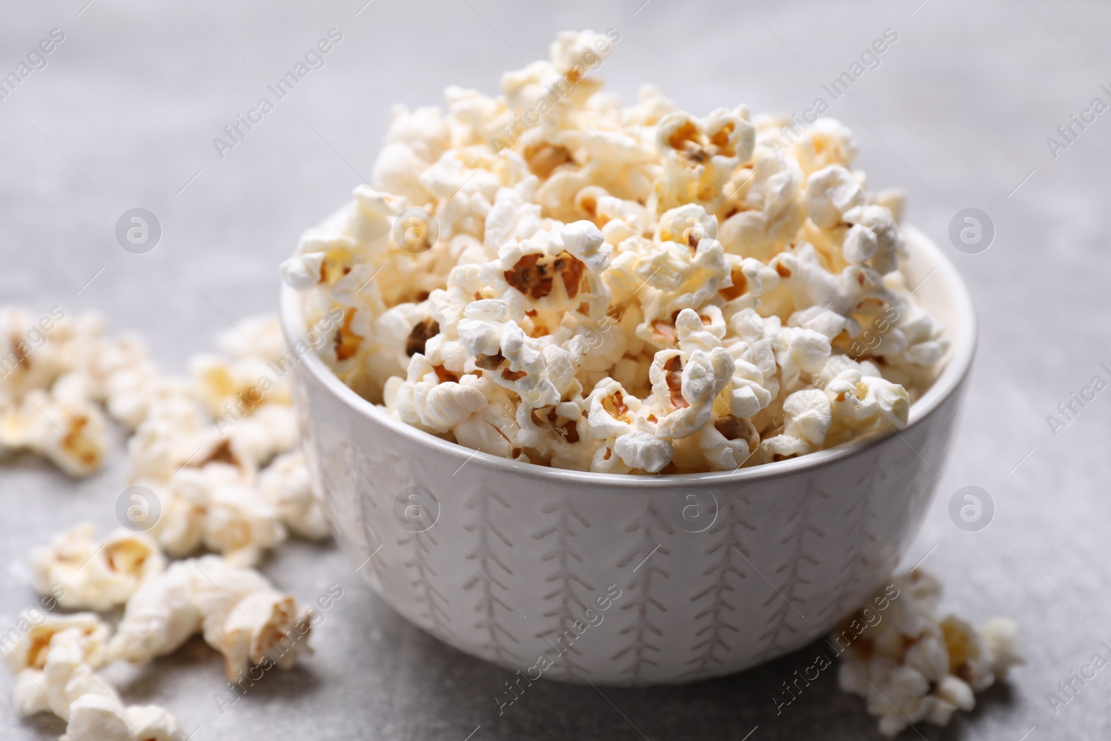 Photo of Bowl of tasty popcorn on grey table, closeup