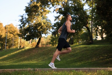 Attractive sporty man jogging along path in beautiful park