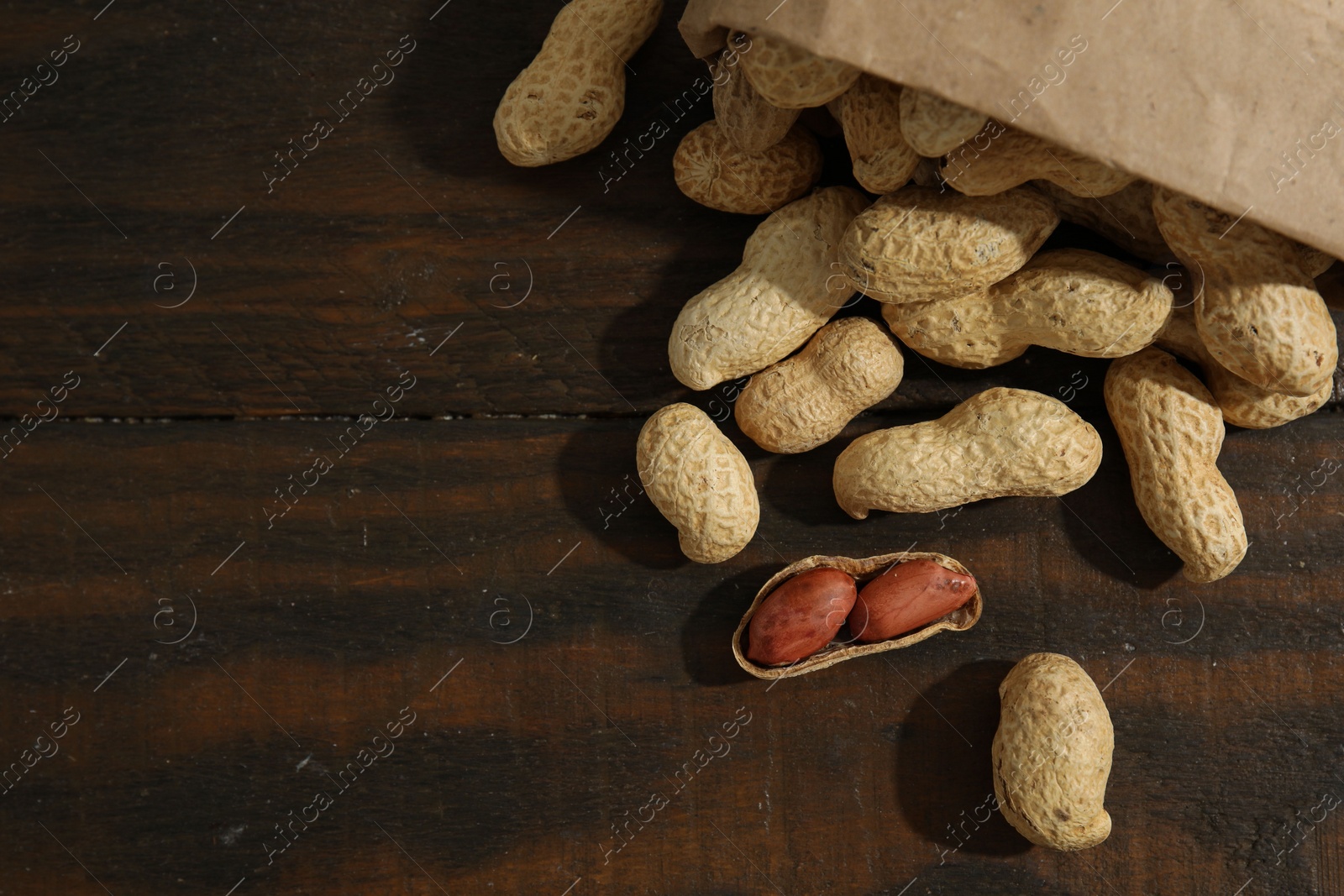 Photo of Paper bag with fresh unpeeled peanuts on wooden table, top view. Space for text