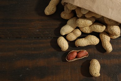 Paper bag with fresh unpeeled peanuts on wooden table, top view. Space for text