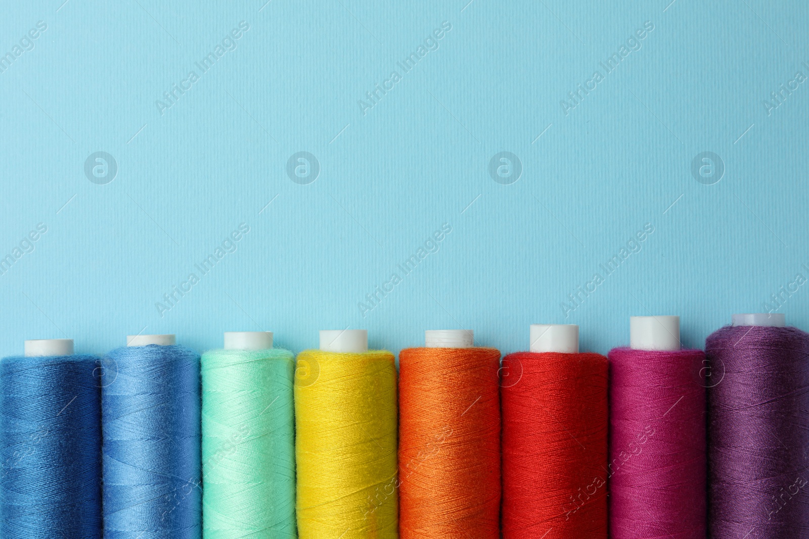 Photo of Set of different colorful sewing threads on light blue background, flat lay. Space for text