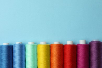 Set of different colorful sewing threads on light blue background, flat lay. Space for text