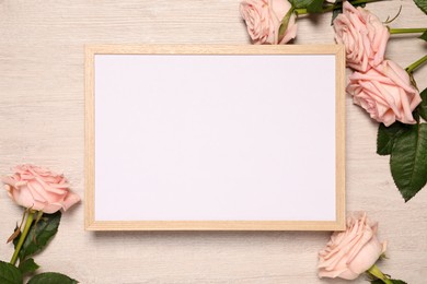 Photo of Empty photo frame and beautiful rose flowers on wooden background, flat lay. Mockup for design