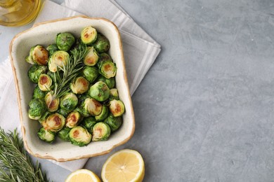 Photo of Delicious roasted Brussels sprouts, rosemary and lemon on grey table, top view. Space for text