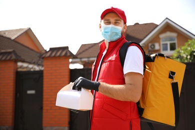 Photo of Courier in protective mask and gloves with order outdoors. Restaurant delivery service during coronavirus quarantine