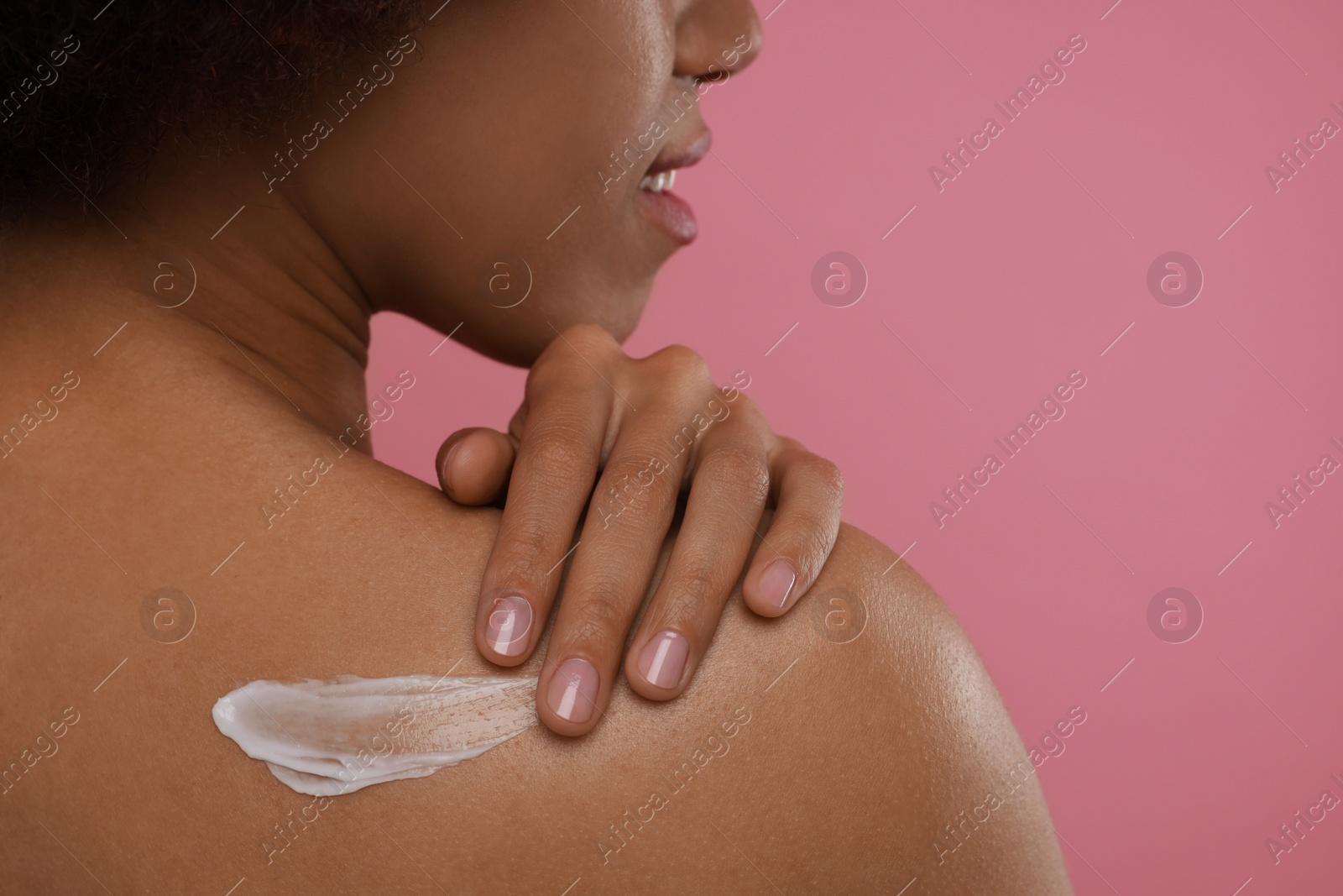 Photo of Young woman applying body cream onto back on pink background, closeup. Space for text