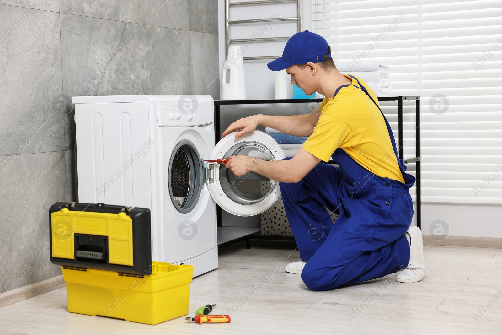 Photo of Young plumber repairing washing machine in bathroom