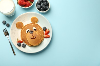 Creative serving for kids. Plate with cute bear made of pancakes and berries on light blue table, flat lay. Space for text