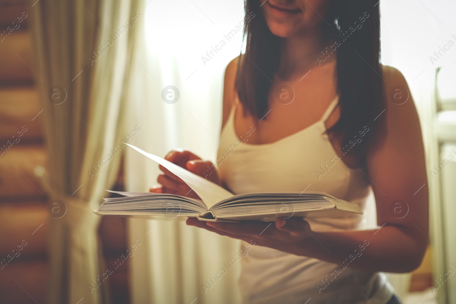 Photo of Young woman reading book at home, closeup