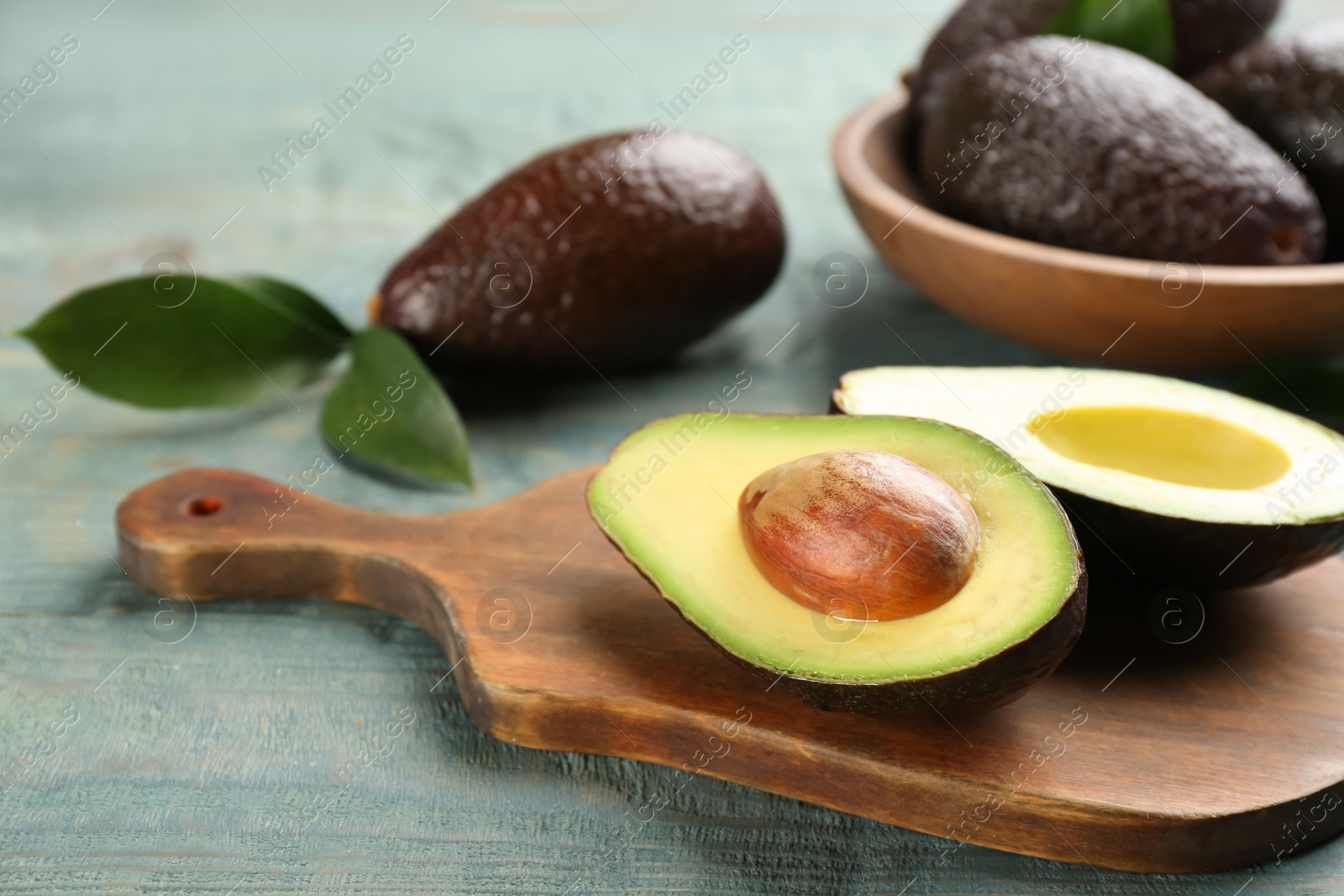 Photo of Cut ripe avocado on light blue wooden table, closeup