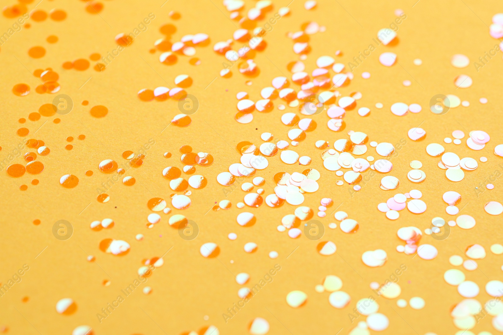 Photo of Shiny bright orange glitter on yellow background, closeup